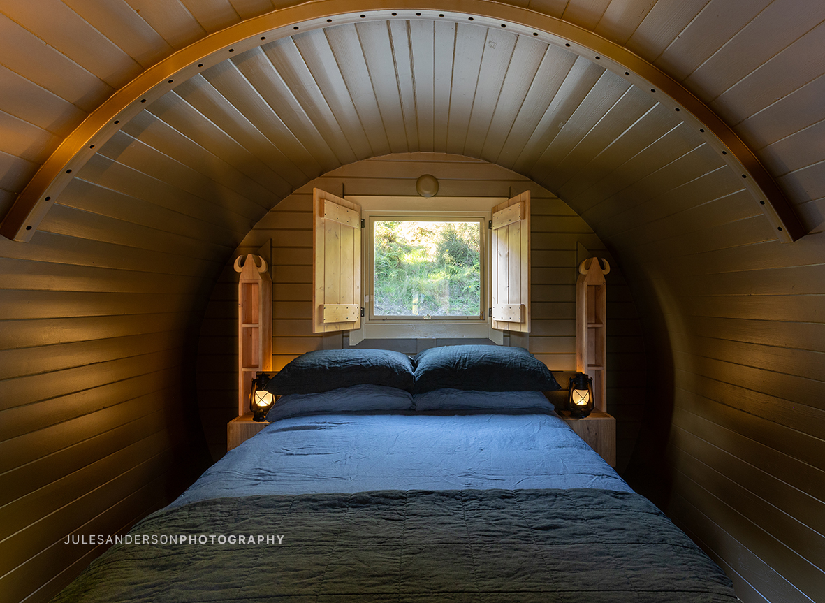 Warmly lit double bed inside the Balder barrel cabin with carved bedside shelves
