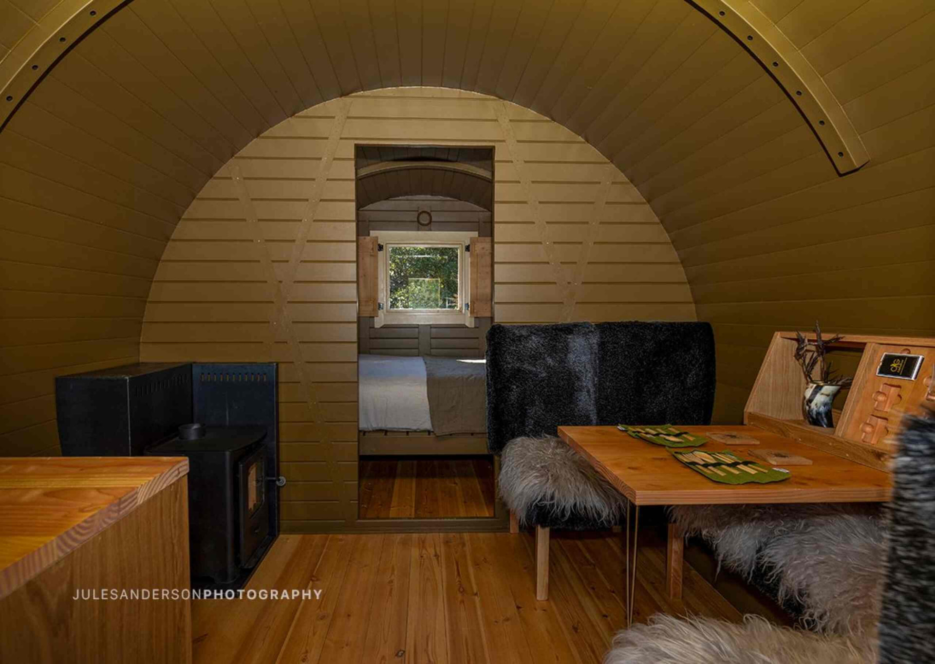 Interior of the Odin barrel cabin with timber dining table, sheepskin seating and a log burner